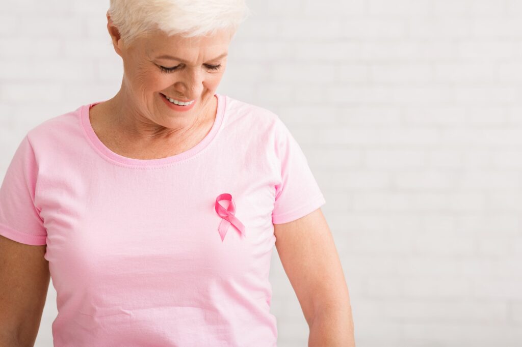 Elderly Woman Looking At Pink Cancer Ribbon On T-Shirt, Indoor