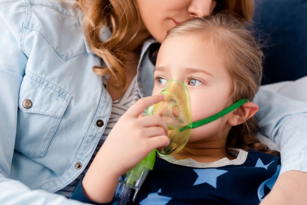 mother kissing asthmatic daughter in respiratory mask